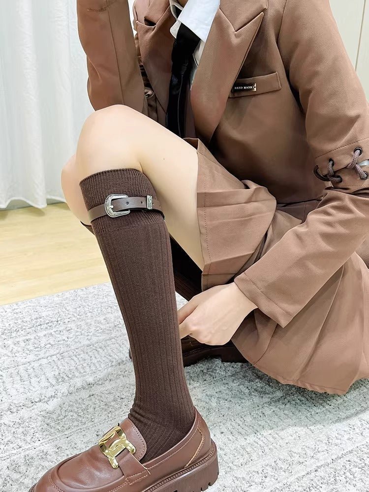 Woman wearing brown knee-high socks with adjustable buckle straps and brown platform loafers, paired with a brown blazer and skirt.