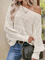 Woman wearing a white open-knit sweater, styled with one shoulder exposed, blue jeans, and a black clutch.