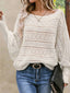 Woman wearing a white open-knit sweater with diamond patterns and bell sleeves, paired with blue jeans and a black belt.