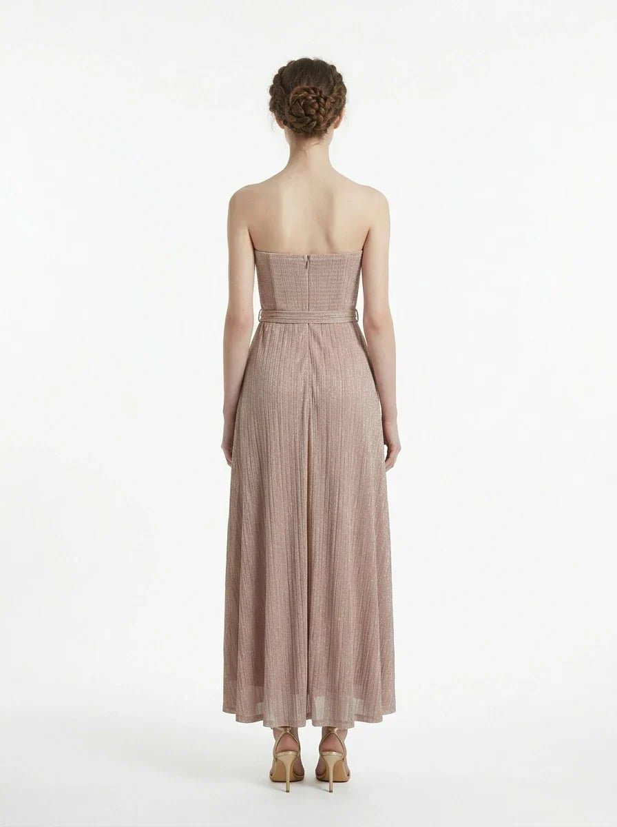 Back view of a woman in a strapless, metallic knit maxi dress with a self-tie belt.