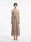 Woman wearing a strapless, metallic knit maxi dress with a self-tie belt, standing against a white background.