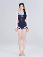 Woman in a navy one-piece swimsuit and sheer white cardigan, standing against a white background.