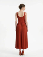 back view of a woman wearing a rust-colored ribbed knit midi dress with a scoop neckline and sleeveless design, standing against a white background