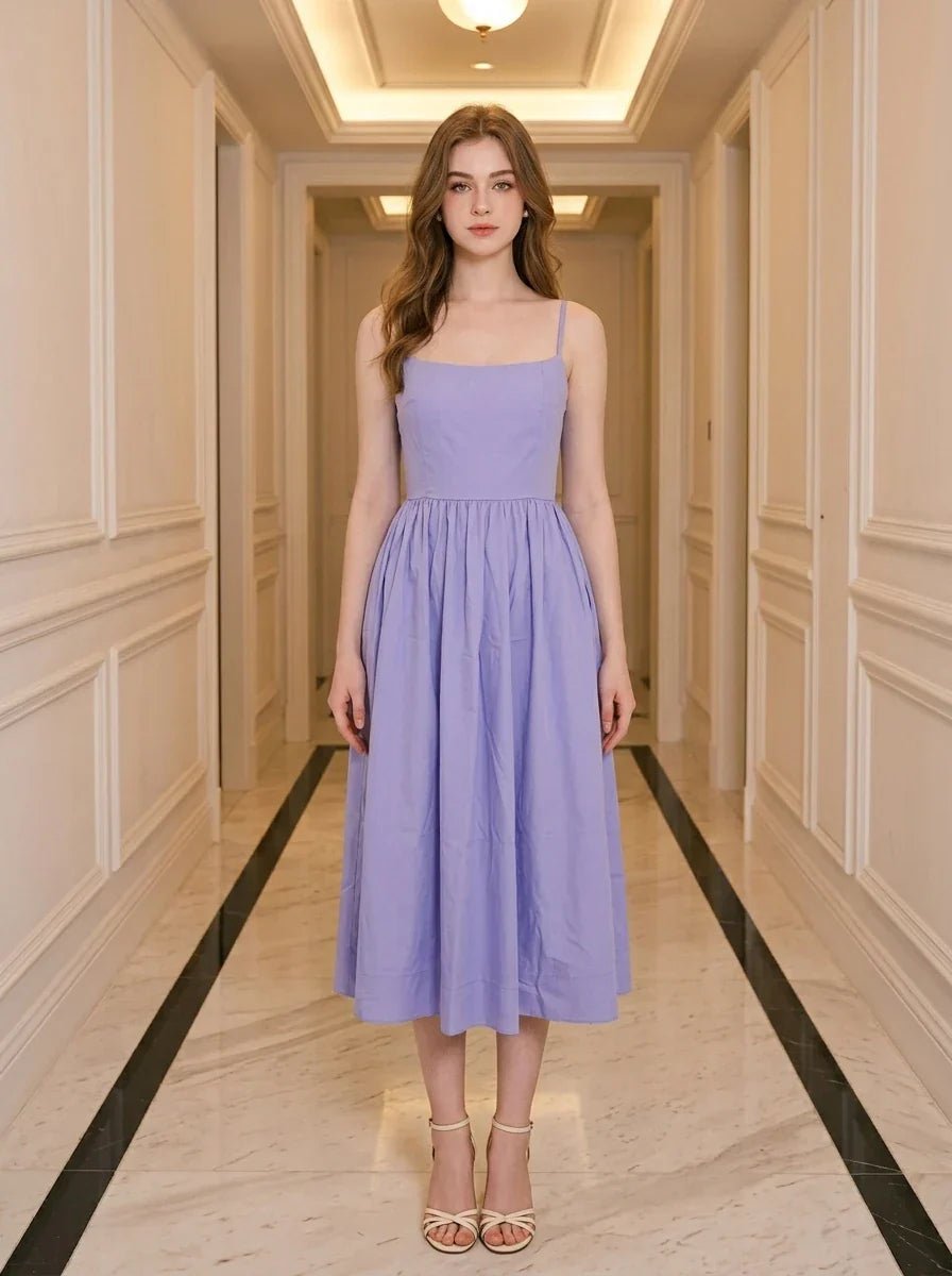 Woman wearing a purple midi dress with spaghetti straps and a square neckline, standing in a hallway.