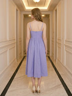 Back view of a woman wearing a purple midi dress with spaghetti straps and a square neckline, standing in a hallway.