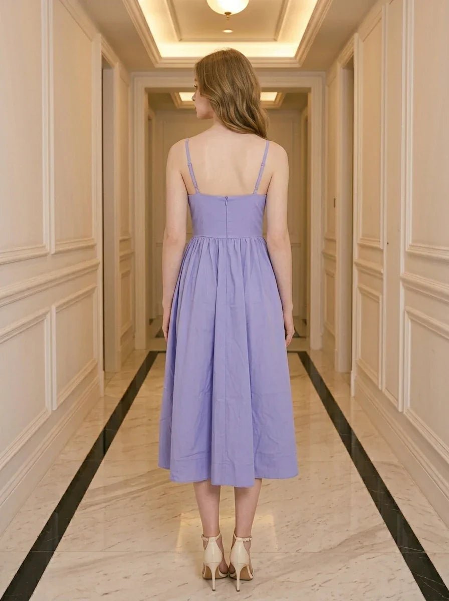 Back view of a woman wearing a purple midi dress with spaghetti straps and a square neckline, standing in a hallway.