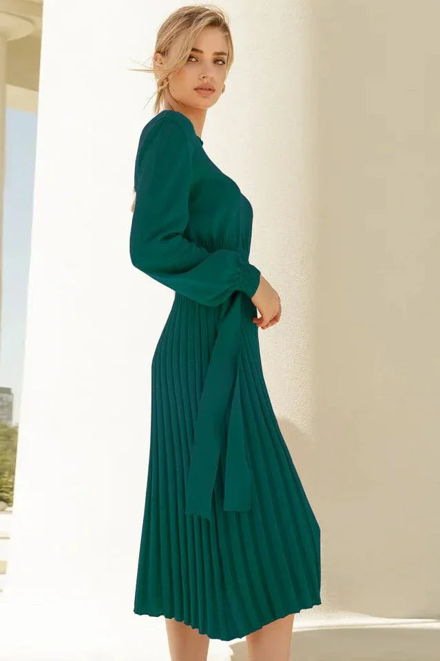 Side view of a woman in a long-sleeved green pleated midi dress with a tie waist.