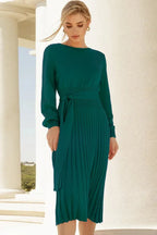 Front view of a woman in a long-sleeved green pleated midi dress with a tie waist.