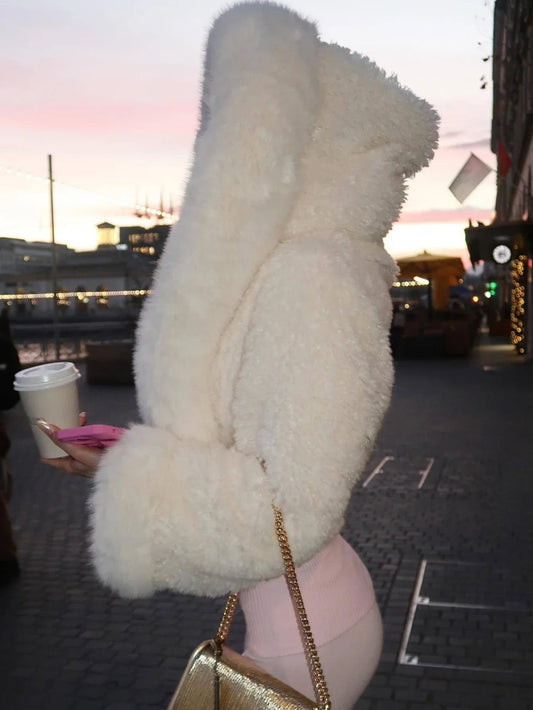 Side view of a woman in a white faux fur cropped jacket with an oversized hood, holding a coffee cup.