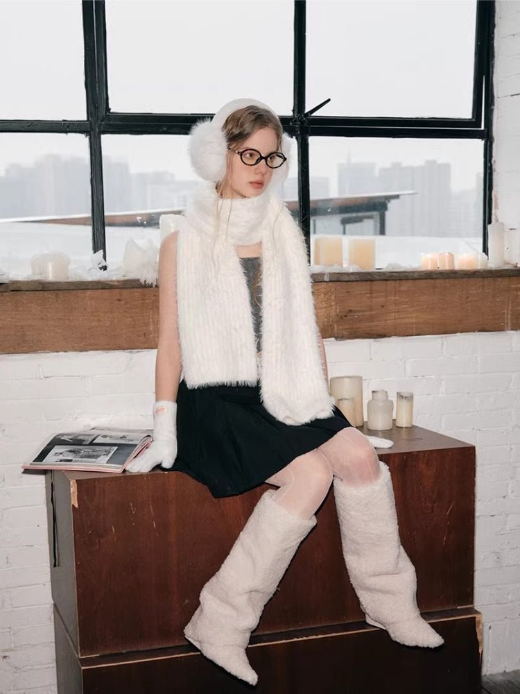 Model sitting on a wooden surface, wearing white fuzzy earmuffs, scarf, gloves, and leg warmers, with a window and candles in the background.