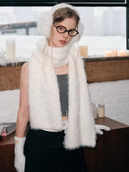 Full body shot of a model wearing white fuzzy earmuffs, scarf, and gloves, paired with a gray top and black skirt.