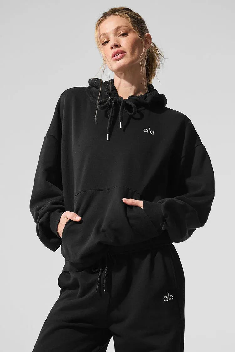 Woman wearing a black cropped hoodie with a kangaroo pocket and embroidered logo.