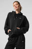 Woman wearing a black cropped hoodie with a kangaroo pocket and embroidered logo.