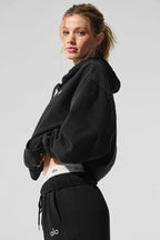 Side view of a woman wearing a black cropped hoodie, showing the waistband of her matching sweatpants.