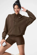 Woman wearing a brown cropped hoodie with a kangaroo pocket and a subtle embroidered logo.