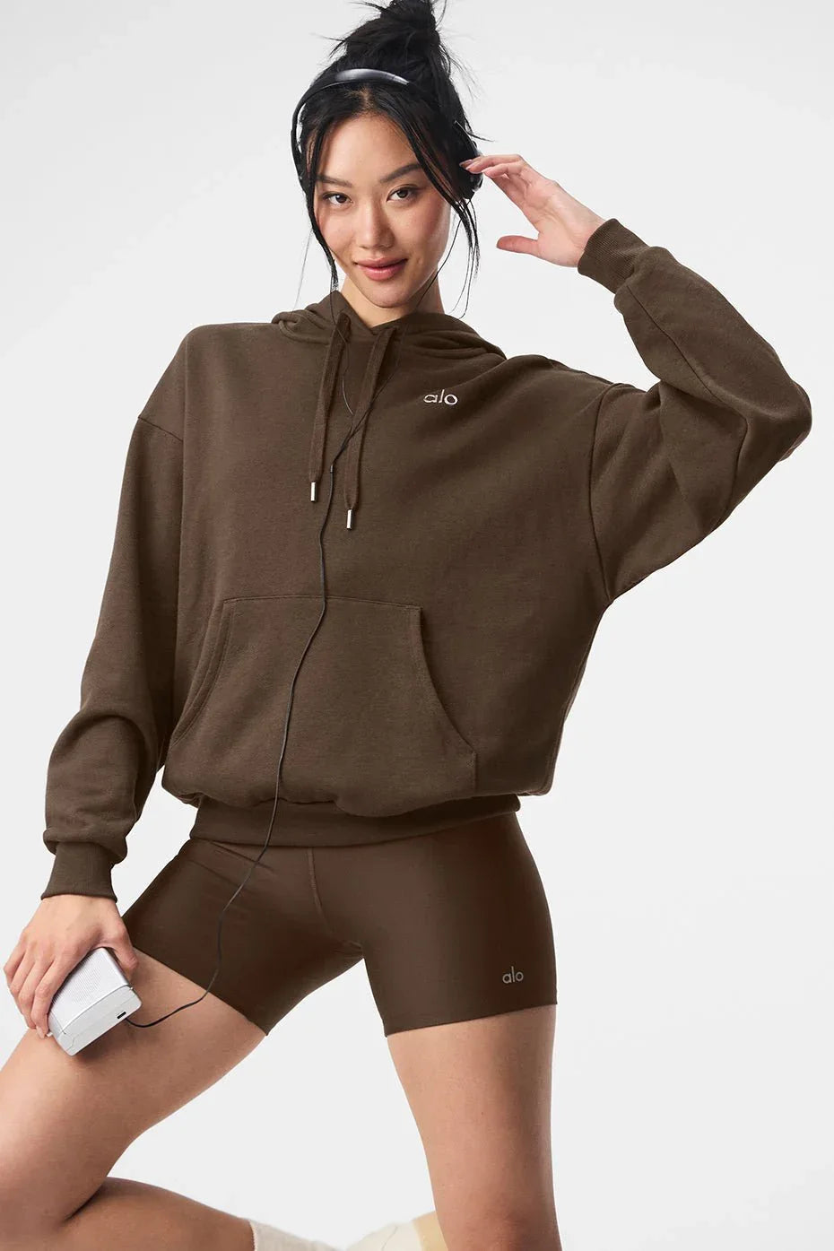 Woman wearing a brown cropped hoodie with a kangaroo pocket and a subtle embroidered logo.