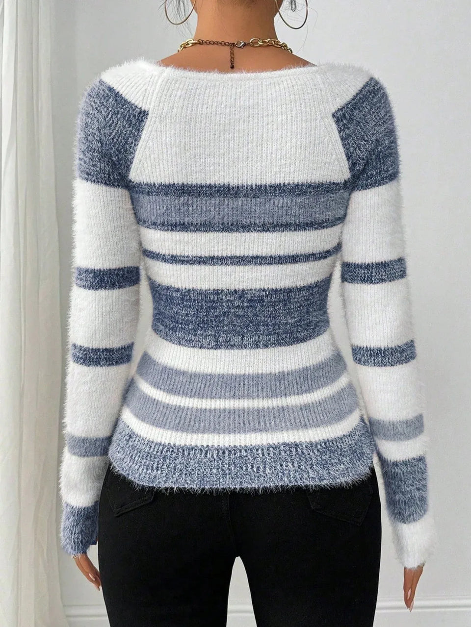 Back view of a woman wearing a blue and white striped fuzzy knit sweater with a square neckline and black pants. Secondary image