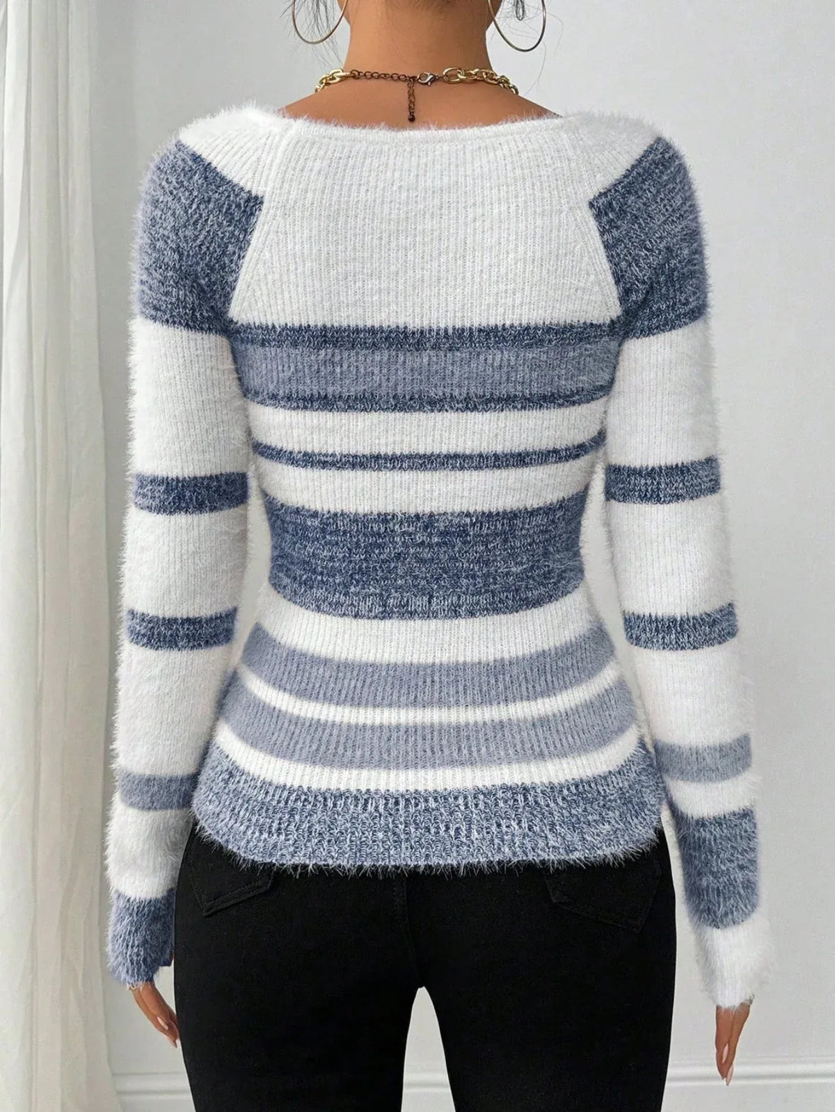 Back view of a woman wearing a blue and white striped fuzzy knit sweater with a square neckline and black pants.