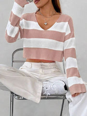 Full body shot of a woman sitting on a chair wearing a pink and white striped cropped sweater with a v-neck, white pants, and white sneakers.