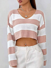 Front view of a woman wearing a pink and white striped cropped sweater with a v-neck and long sleeves, paired with white pants.