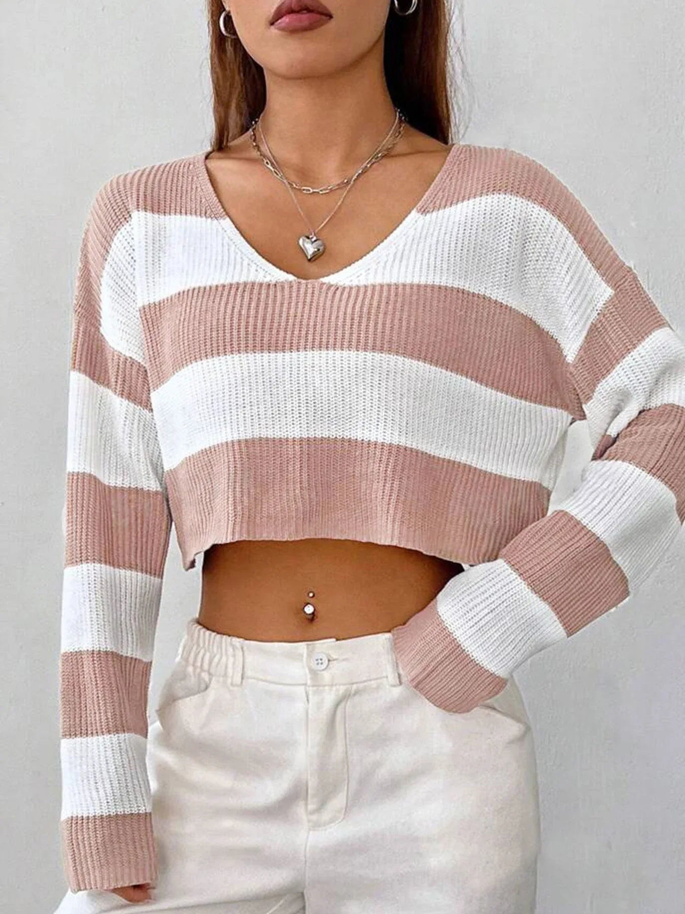 Close-up front view of a woman wearing a pink and white striped cropped sweater with a v-neck, showcasing the neckline and cropped length.