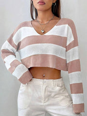 Front view of a woman wearing a pink and white striped cropped sweater with a v-neck and long sleeves, with one hand on her hip.