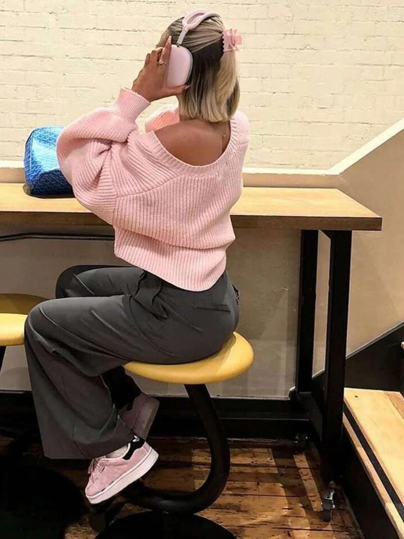 Woman from behind wearing a pink knit cardigan off the shoulder with grey pants.