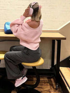 Woman from behind wearing a pink knit cardigan off the shoulder with grey pants.
