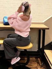 Woman from behind wearing a pink knit cardigan off the shoulder with grey pants.