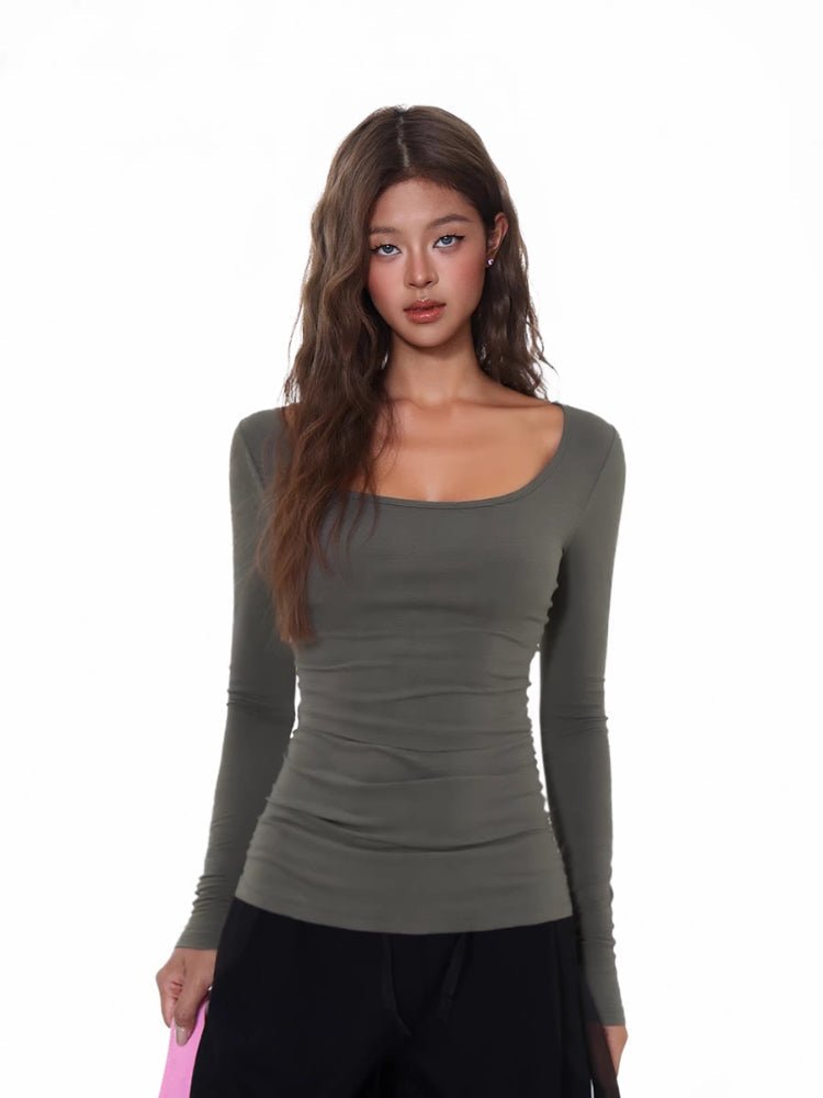 Model wearing a fitted, grey, long-sleeved, scoop neck top with a ribbed texture and ruched side detail.