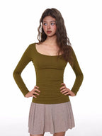 Model wearing a fitted, olive green, long-sleeved, scoop neck top with a ribbed texture and ruched side detail.