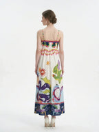 Woman wearing a white sleeveless maxi dress with a colorful graphic print and spaghetti straps, back view