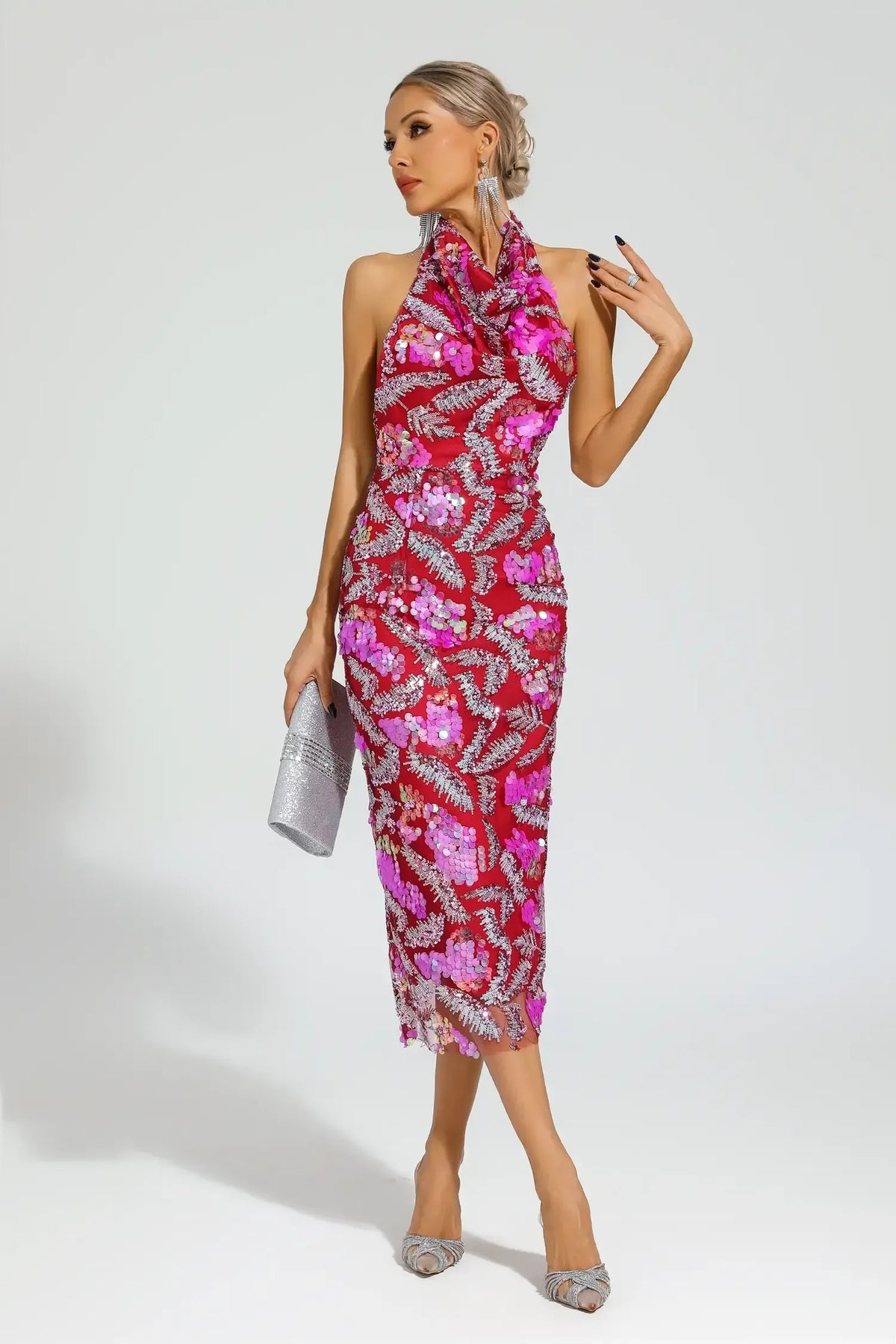 Woman wearing a red sequined halter midi dress with floral appliques, holding a silver clutch.
