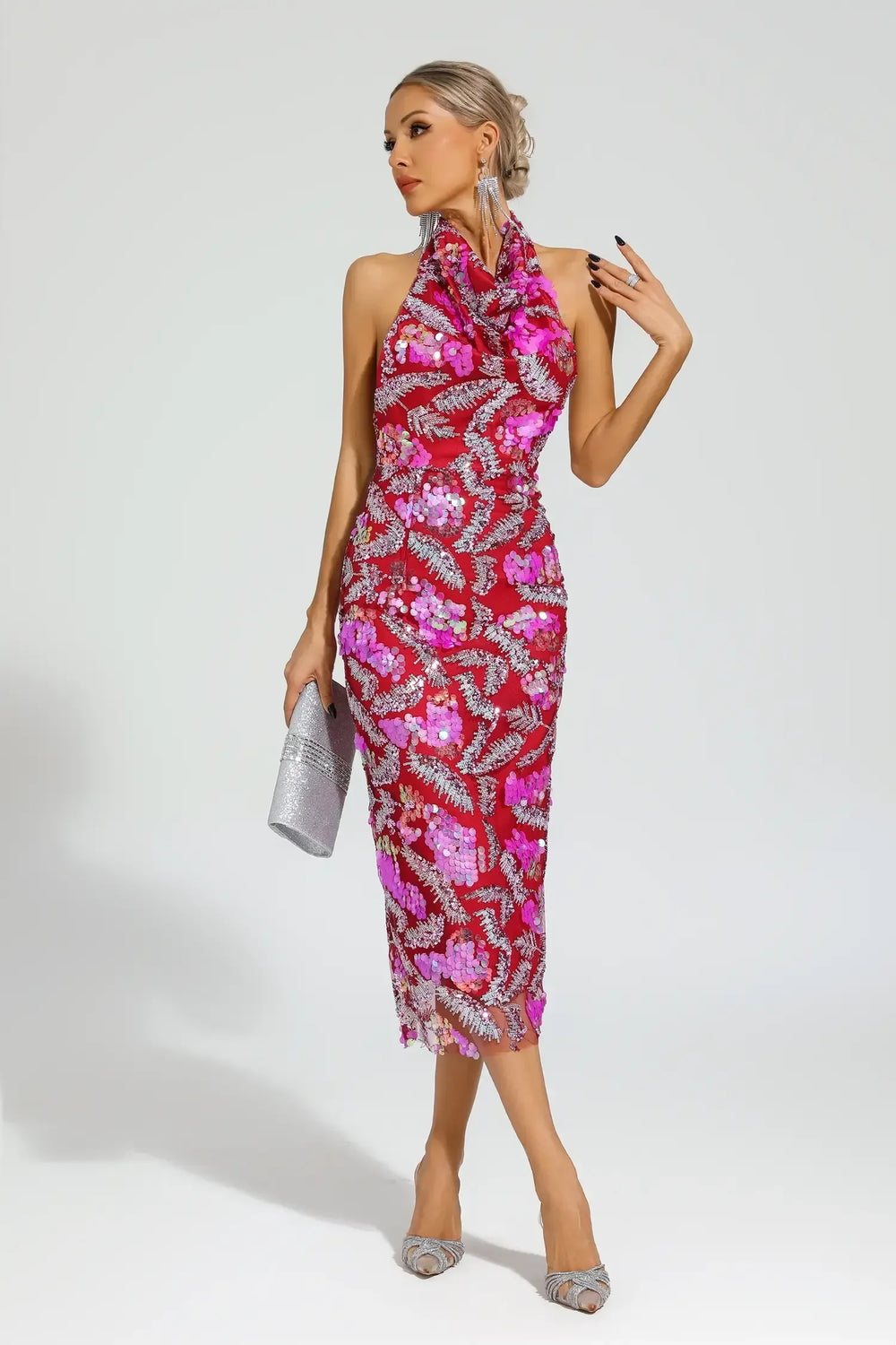 Woman wearing a red sequined halter midi dress with floral appliques, holding a silver clutch.